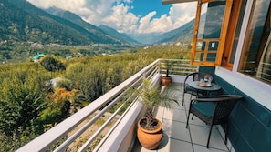 Un balcón con vistas a un paisaje montañoso, una planta en maceta y una mesa con sillas.
