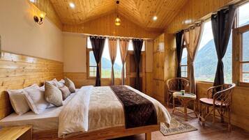 Une pièce en bois avec un lit, une chaise, une petite table et une vue sur les montagnes par les fenêtres.
