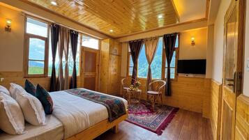 Una habitación con paneles de madera, una cama, dos sillas, una mesita con flores y un televisor montado en la pared.