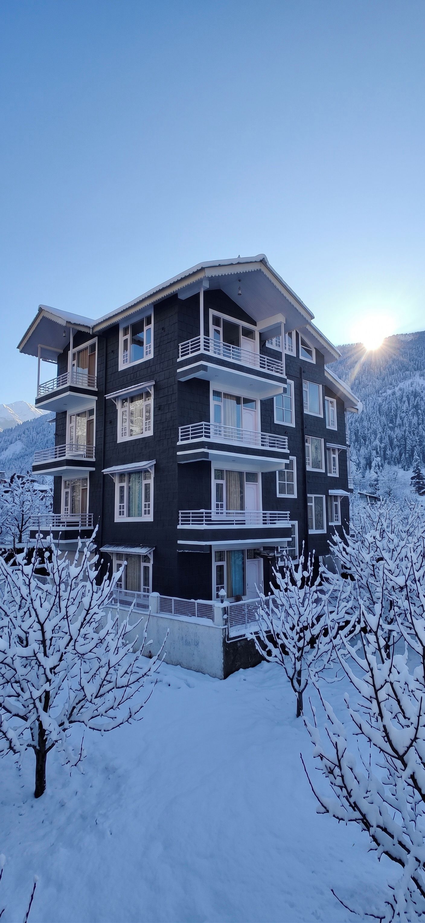Un edificio de varios pisos con balcones, rodeado de árboles nevados y montañas.