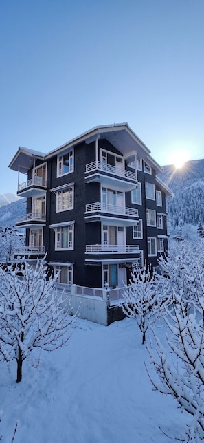 Un edificio de varios pisos con balcones, rodeado de árboles nevados y montañas.