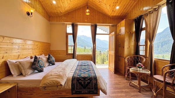 Una habitación de madera con una cama, una silla, una mesa y vistas a las montañas.