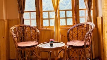 A cozy room with wooden walls and a sloped ceiling, featuring two wicker chairs, a small round table, and a colorful carpet.