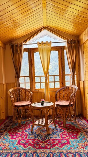 Una habitación acogedora con paredes de madera y techo inclinado, que incluye dos sillas de mimbre, una mesita redonda y una alfombra colorida.