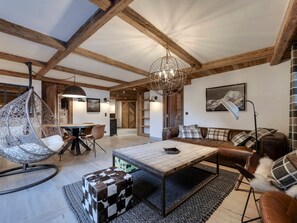 A spacious living area with a wooden ceiling, a hanging chair, a sofa with cushions, a coffee table, and a floor lamp. - Apartment in Val d'Isère - 6 guests (Val-d'Isère)