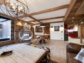 A rustic interior with exposed wooden beams, a hanging chair, a dining table, and a leather sofa. - Apartment in Val d'Isère - 6 guests (Val-d'Isère)