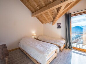 A bedroom with two beds, a wooden ceiling, a window with a view of mountains, and a small table. - Chalet panoramic view - 9 guests (La Toussuire)