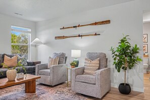 A modern living room with grey sofas, a coffee table, and a potted plant. - 5BR/3BA Gem State Getaway | Game Room + Yard (Nampa)