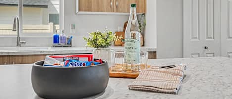 A kitchen with a marble countertop, a bowl of snacks, a bottle of Cascade Mountain water, and a potted plant.