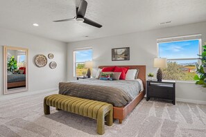 A bedroom with a bed, a bench, a ceiling fan, and a window with a view. - 5BR/3BA Gem State Getaway | Game Room + Yard (Nampa)