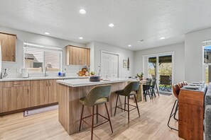 A modern kitchen with wooden cabinets, a marble countertop, and a bar area with stools. - 5BR/3BA Gem State Getaway | Game Room + Yard (Nampa)