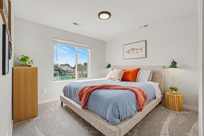 A bedroom with a bed, a window, a bedside lamp, and a framed picture on the wall. - 5BR/3BA Gem State Getaway | Game Room + Yard (Nampa)
