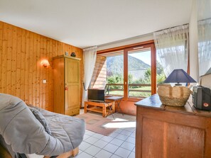 A cozy room with wooden walls, a bed, a TV, a table with a lamp, and a view of the outdoors. - Central apartment in Morzine - 5 guests (Morzine)