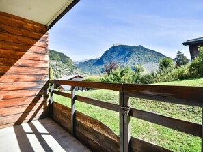 Un balcon en bois, doté d’une balustrade en métal, qui offre une vue sur un paysage montagneux.