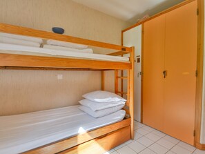 Een slaapkamer met een stapelbed van hout, een enkel bed en een kledingkast.
