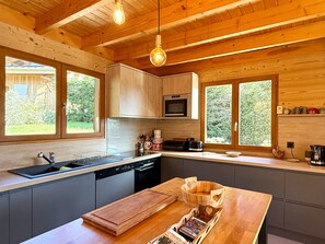 A modern kitchen with wooden cabinets, a built-in oven, and a large island with a cutting board and wooden bowls. - Renovated chalet, exceptional views - 8 guests (Les Gets)