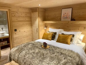 Una habitación de madera con una cama, una mesita de noche, un cuadro enmarco y una ventana.