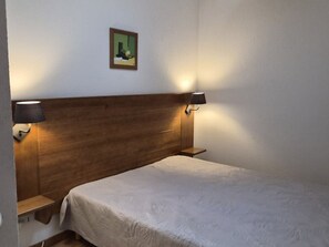 Ein Hotelzimmer mit einem hölzernen Kopfteil, zwei Nachttischlampen, einem Bett mit weißer Bettdecke und einem kleinen Gemälde an der Wand.
