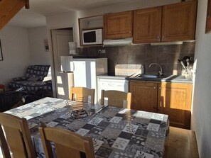 A compact kitchen with wooden cabinets, a microwave, a dishwasher, and a sink. There is a table with a patterned tablecloth and two chairs. - Quiet duplex apartment - 8 guests (Orcières Merlette)