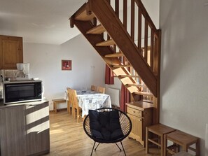 A kitchen with a microwave, wooden cabinets, a dining table with chairs, and a staircase. - Quiet duplex apartment - 8 guests (Orcières Merlette)