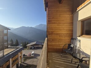 A balcony with a view of mountains, a chair, and a building with a window. - Quiet duplex apartment - 8 guests (Orcières Merlette)