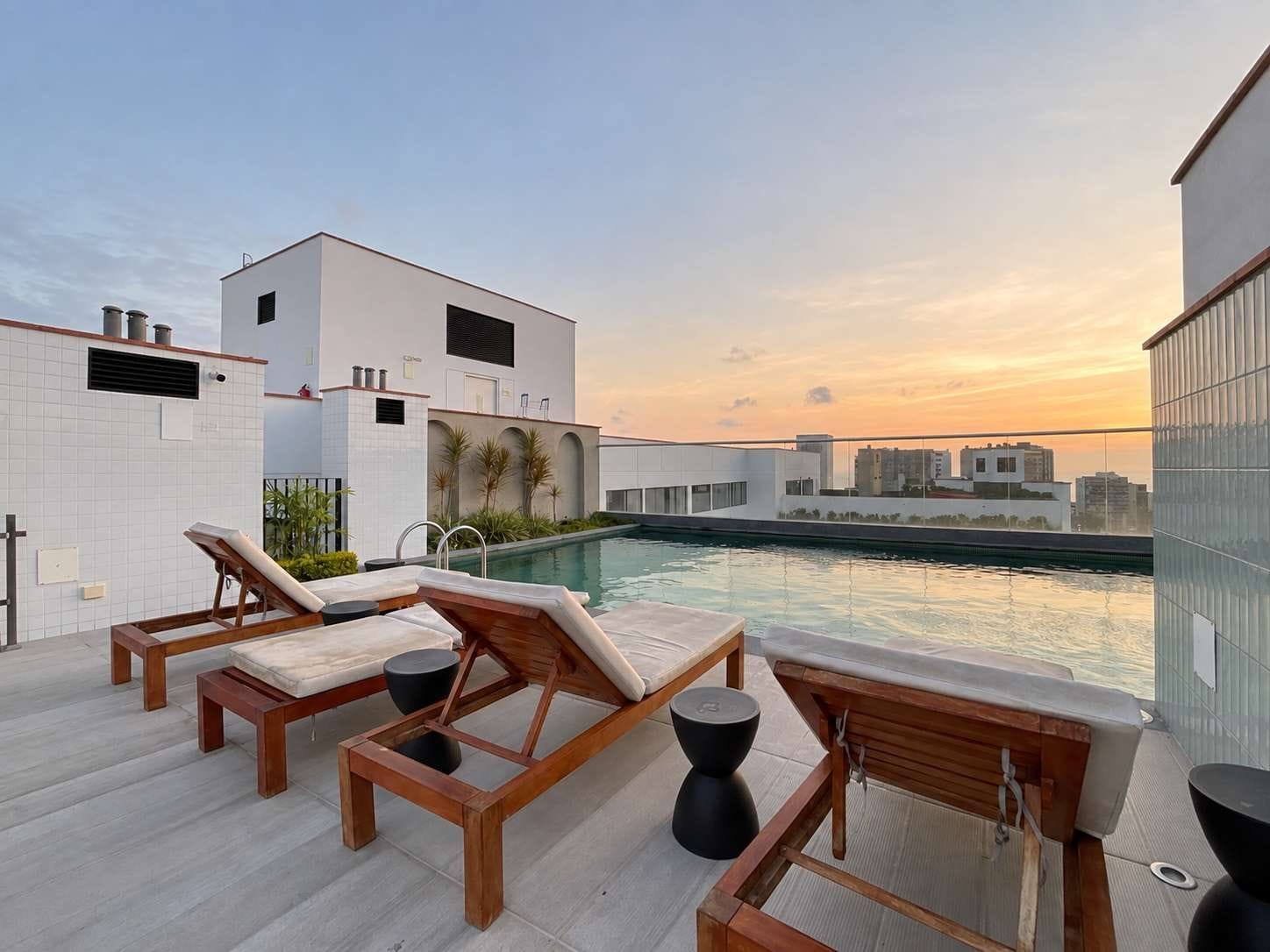 A rooftop pool area with lounge chairs and a view of the cityscape at sunset.
