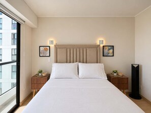 Quarto de hotel com uma cama grande, duas mesas de cabeceira, uma luminária de chão e obras de arte nas paredes.