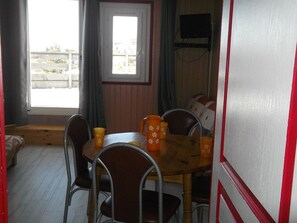 Ein Essbereich mit Holztisch und Metallstühlen, einem Fenster mit Vorhängen und einem an der Wand befestigten Fernseher.