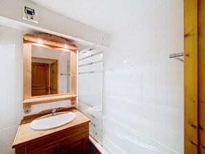 Une salle de bain avec un meuble-lavabo en bois, un lavabo blanc, un miroir avec un cadre en bois et un espace douche.