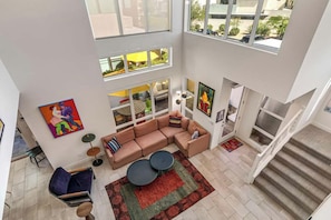 A spacious living area with a sectional sofa, a coffee table, and a rug. There are multiple windows allowing natural light and views of the outside. - Spectacular Living in Palm Springs' Coveted Vibe Community (Palm Springs)