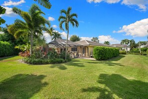 A residential property with a covered patio, a lawn, and tropical vegetation. - NEW! 3BR Park Shore Retreat w/ Large Pool & Patio (Naples)