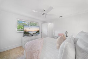 A bedroom with a bed, a ceiling fan, a window with blinds, a TV, and a door. - NEW! 3BR Park Shore Retreat w/ Large Pool & Patio (Naples)