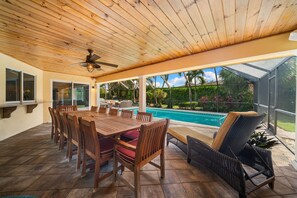 A covered patio with a pool, wooden furniture, and a ceiling fan. - NEW! 3BR Park Shore Retreat w/ Large Pool & Patio (Naples)