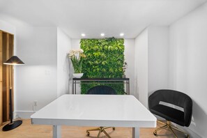 Quarto moderno com uma mesa branca, uma cadeira preta, uma parede coberta por plantas verdes e um pequeno vaso com planta sobre a mesa.