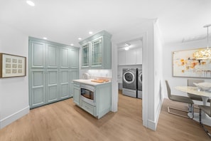 A modern kitchen with light blue cabinets, a central island, and a dining area with a round table and chairs. - NEW! 3BR Park Shore Retreat w/ Large Pool & Patio (Naples)