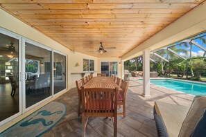 A covered patio with a wooden table and chairs, a ceiling fan, and a view of a swimming pool. - NEW! 3BR Park Shore Retreat w/ Large Pool & Patio (Naples)