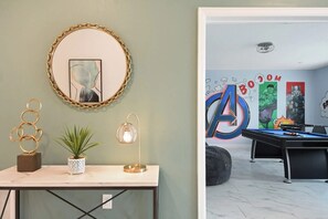 Ein Zimmer mit einem Marmortisch, einem spiegelnden Spiegel mit goldener Rahmen, einer Topfpflanze und einer modernen Lampe.