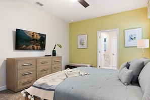 A bedroom with a bed, a dresser, a painting, and a door leading to a bathroom. - Stunning 9BR Villa Near Disney Storey Lake (Kissimmee)