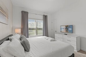 A hotel room with a bed, a TV, a desk, and a window with curtains. - Modern Home w/ Private Pool Near Disney (Kissimmee)