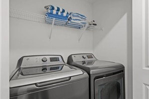 A laundry area with two front-loading washing machines and a shelf above holding folded towels. - Modern Home w/ Private Pool Near Disney (Kissimmee)