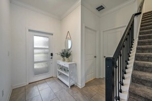 A hallway with a white door, a small white console table with plants, and a staircase with black railings. - Townhome w/ Private Pool 10min From Disney (Kissimmee)