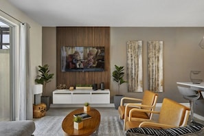 Un salon moderne avec un téléviseur, un mur recouvert de panneaux en bois, un meuble de rangement blanc pour appareils électroniques, deux fauteuils, une table basse et un tapis à motifs.