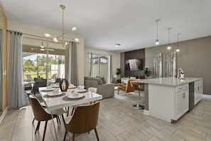 A modern kitchen with a central island, dining area with chairs and a table set for four, and a living area with a sofa and TV. - Themed Home w/ Private Pool (Davenport)