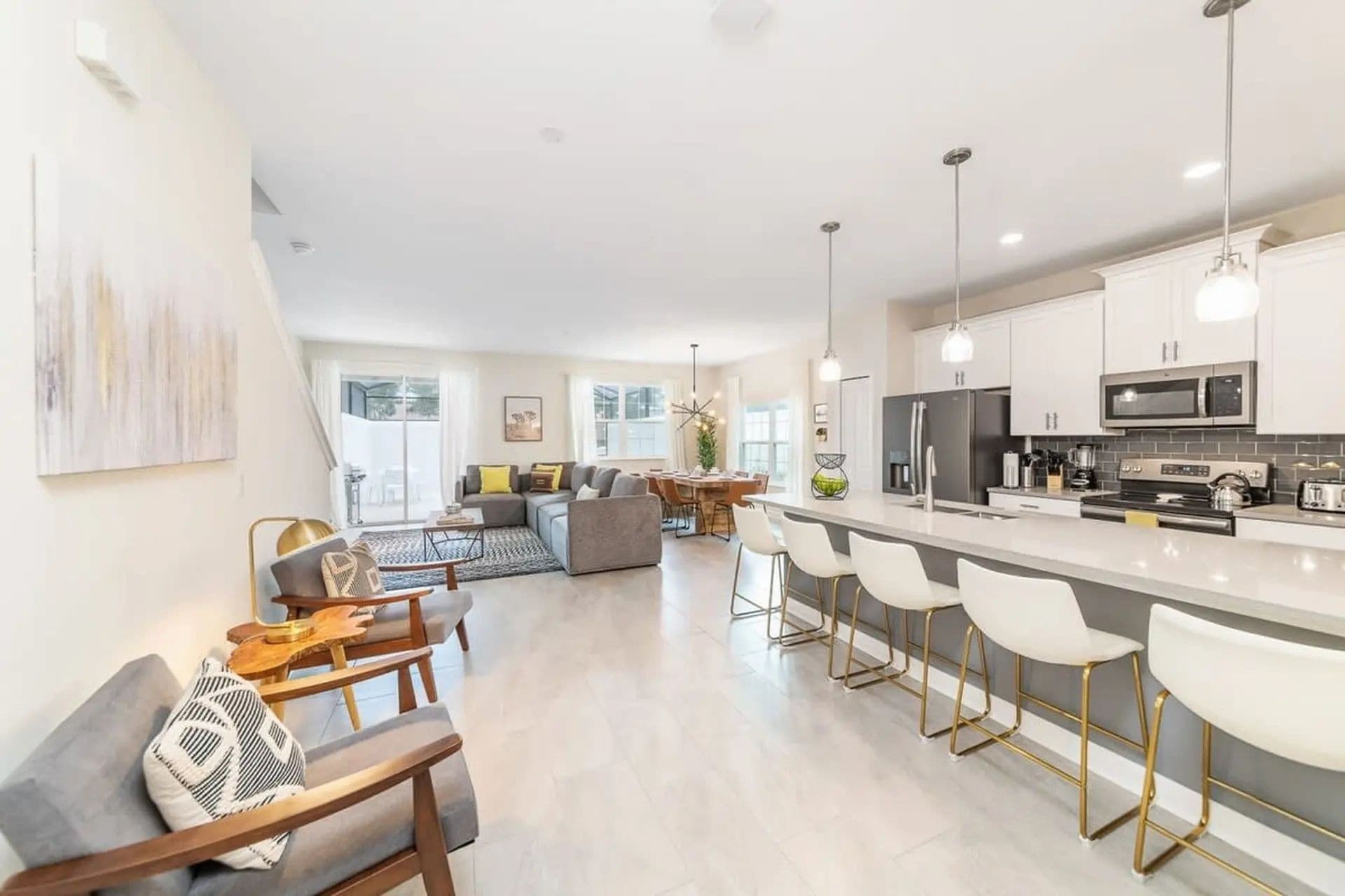 A modern kitchen with a central island, bar stools, and a dining area with a sofa and chairs.