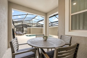 Ein überdachter Außenbereich mit rundem Tisch und Stühlen, einem Pool und Liegestühlen.