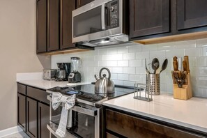 A modern kitchen with dark cabinets, a stainless steel microwave, a kettle, a blender, and a coffee maker. - 4BR Home w/ Private Pool & Disney-themed Rooms (Kissimmee)