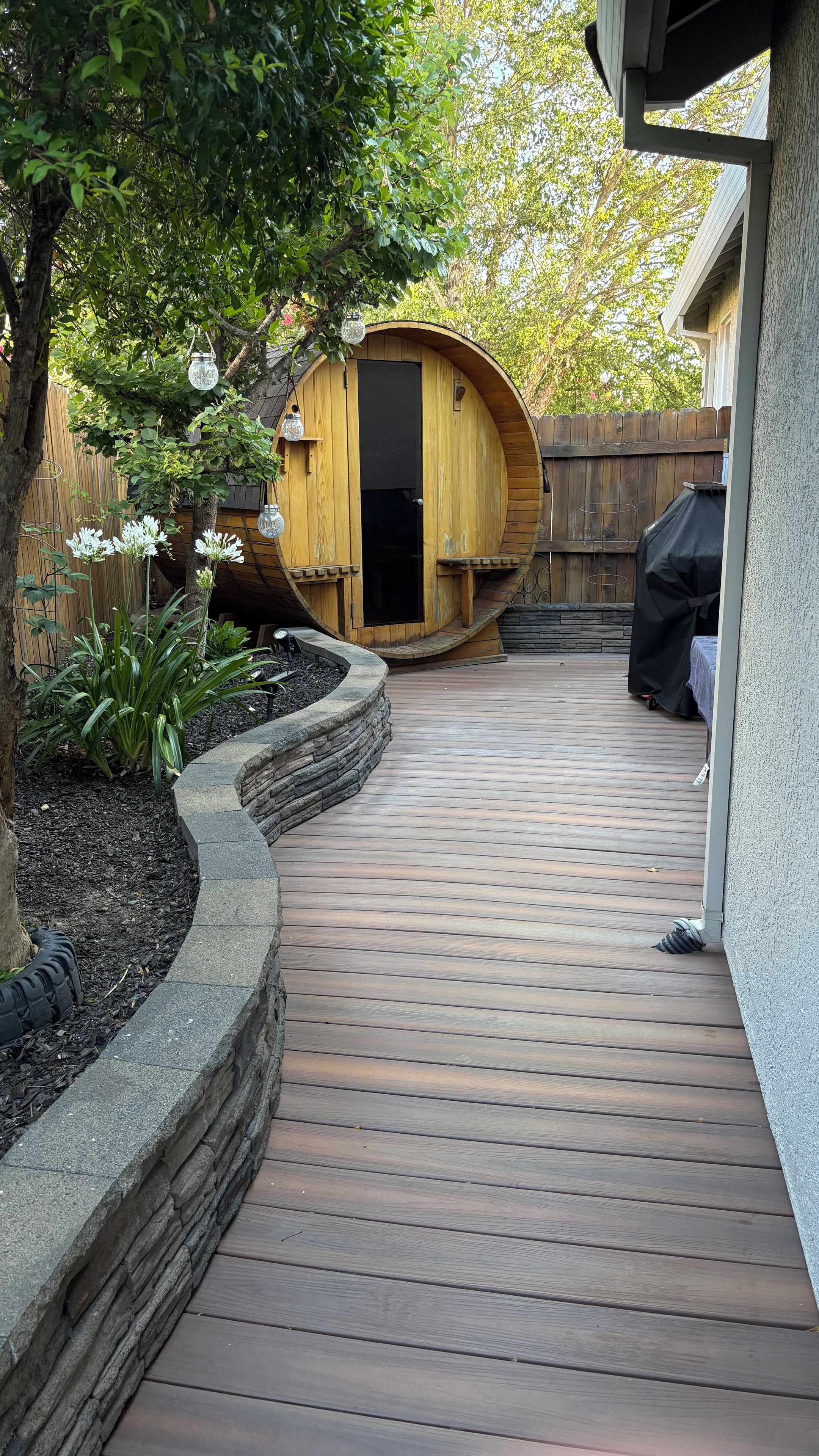 A wooden deck leading to a circular wooden structure, surrounded by a wooden fence and a tree.