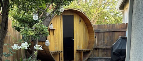 A wooden deck leading to a circular wooden structure, surrounded by a wooden fence and a tree.
