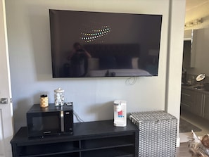 A flat-screen TV mounted on a wall, a black microwave, a white coffee maker, and a wicker basket on a black countertop. - Beautiful home in Antelope with private room, and private access. (Antelope)