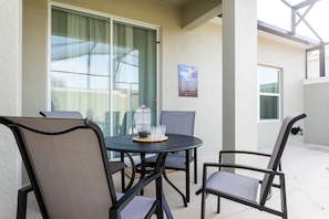 An outdoor patio with a round table and four chairs, a glass door, and a sign indicating a pool and hole 9. - 5BR Home w/ Private Pool & Disney-themed Rooms (Kissimmee)